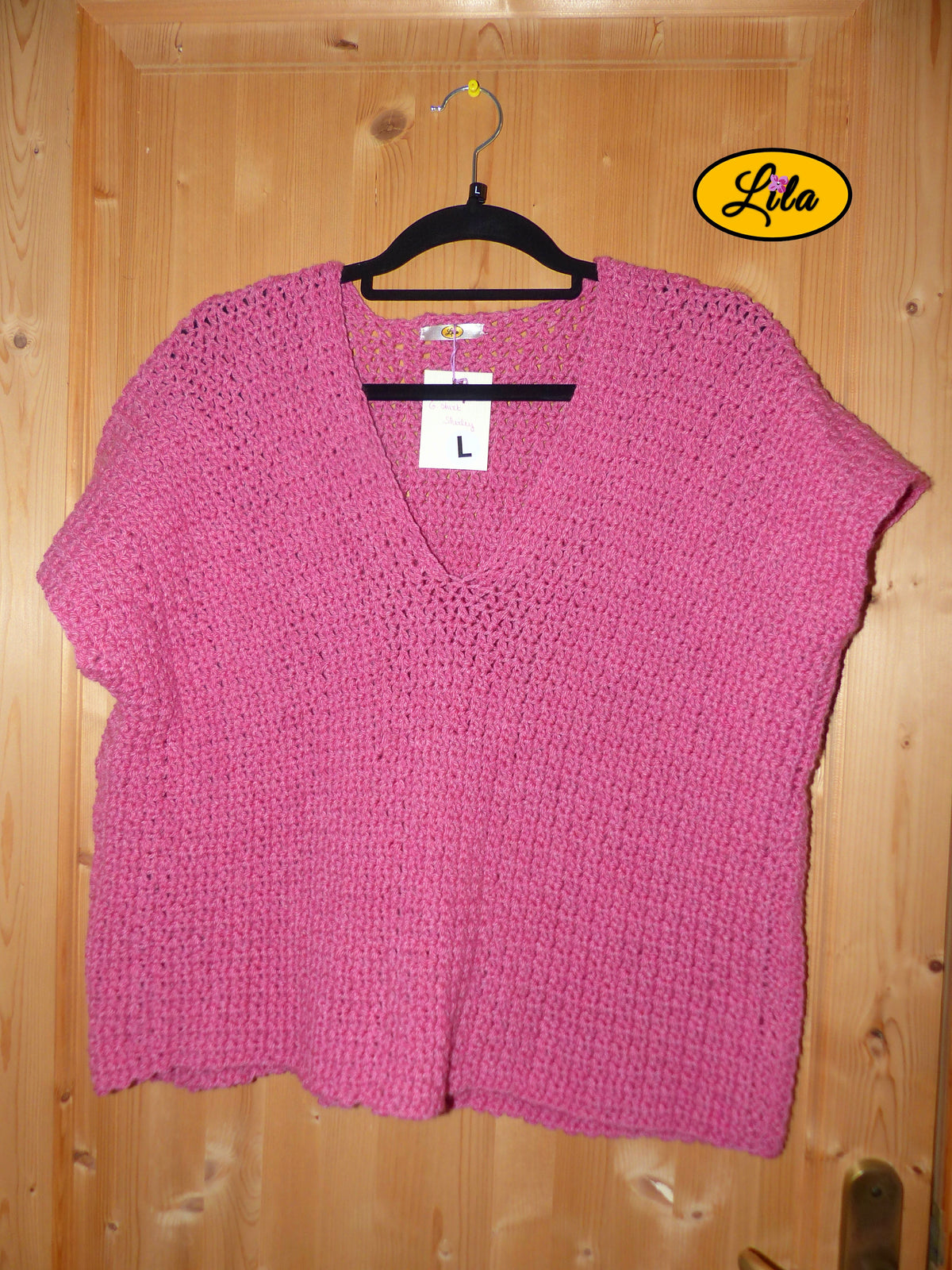 T-shirt rose crocheté à la main en laine acrylique, taille L, présenté sur cintre accroché à une porte, vue de face