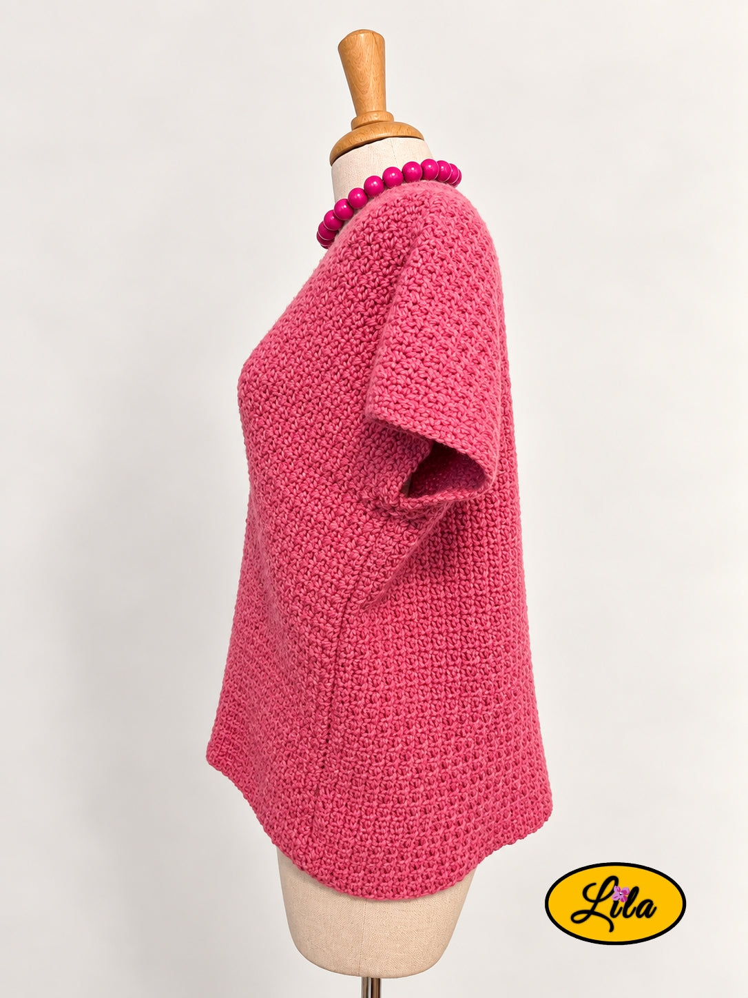 T-shirt rose en crochet fait main en laine acrylique, taille L, vu de profil gauche sur mannequin de couture, mettant en valeur le point crocheté et la coupe du vêtement