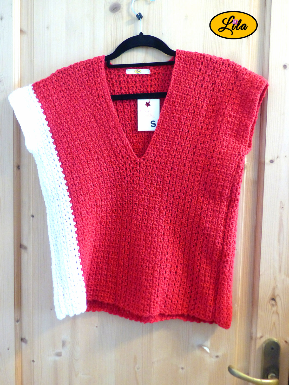 T-shirt rouge crocheté à la main en laine acrylique, taille S, avec bande blanche sur le côté droit, suspendu sur cintre vue de face