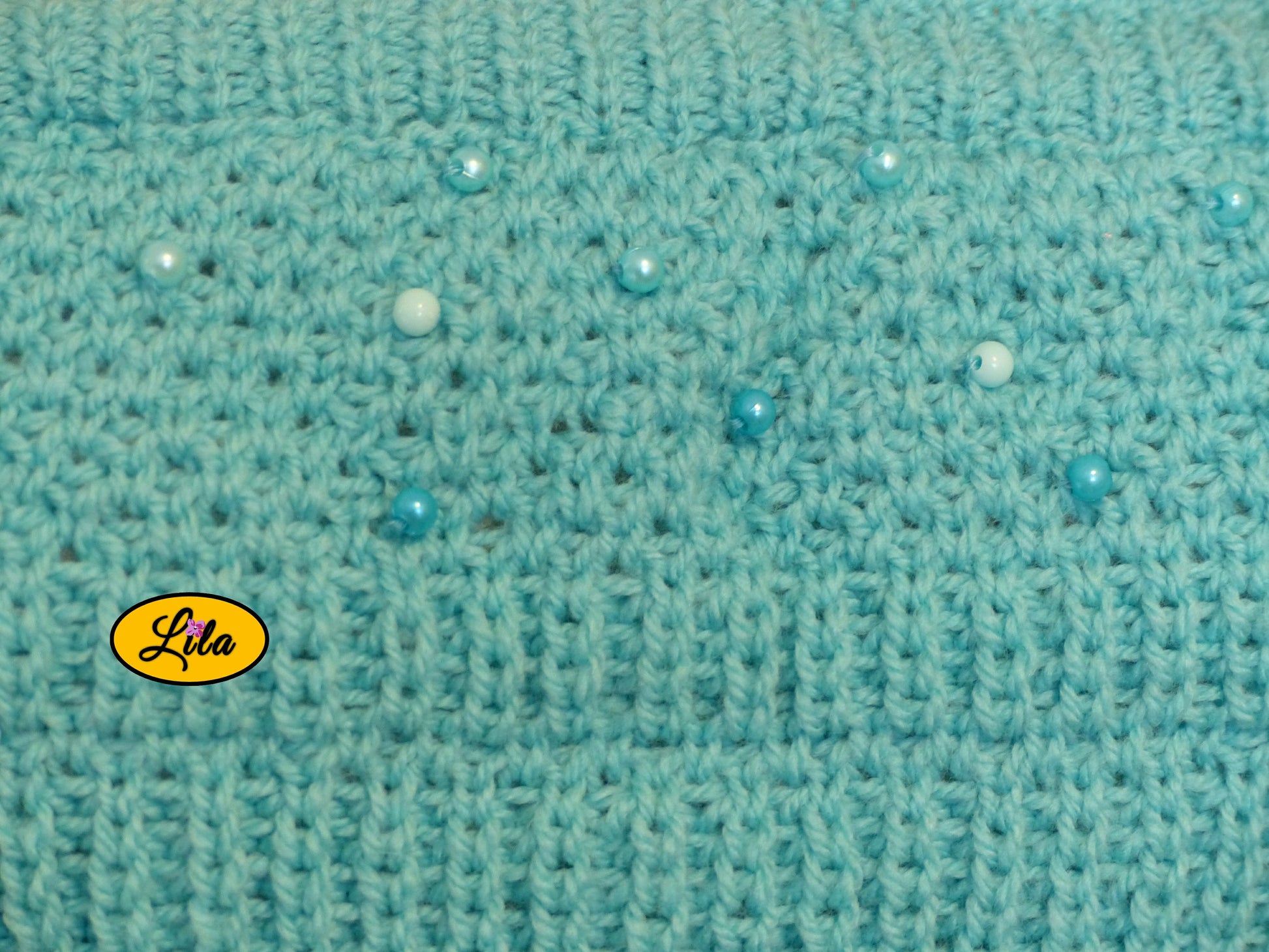 Zoom sur les perles cousues du top Augustine bleu tricoté à la main détail élégant et artisanal