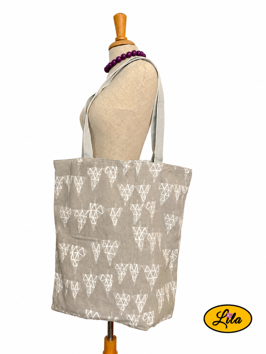 Tote bag en tissu gris à motifs de sapins graphiques gris clair porté sur mannequin de couture sur fond blanc avec sangles grises style moderne et artisanal