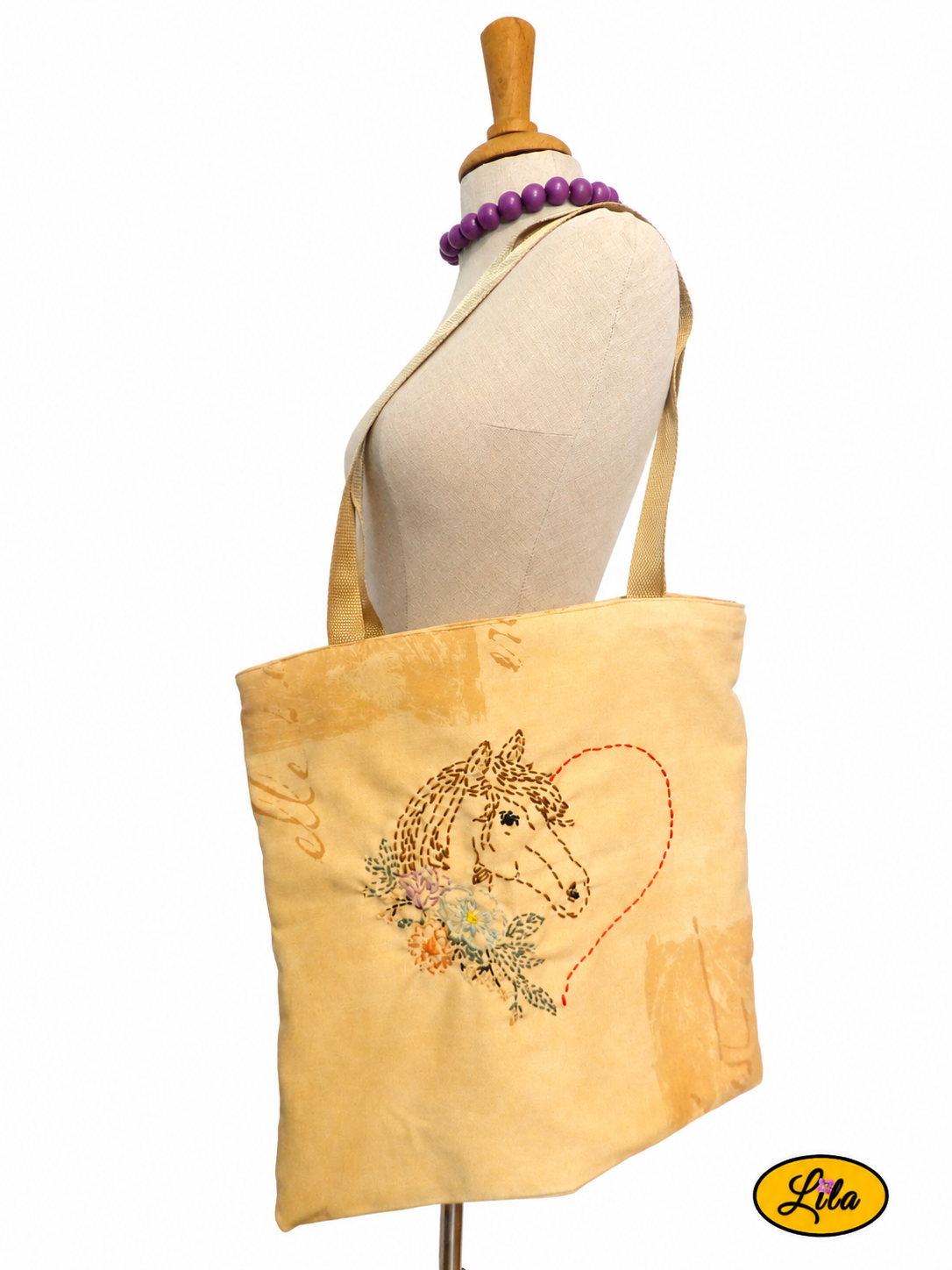 Tote bag jaune avec broderie artisanale représentant un cœur terminé par une tête de cheval et décor floral porté sur mannequin de couture sur fond blanc style équestre et artisanal