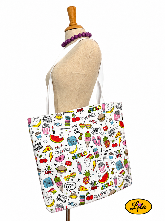 Tote bag en tissu à motifs girly avec rouges à lèvres, appareils photo et bisous porté sur mannequin de couture sur fond blanc avec sangles blanches style féminin et artisanal