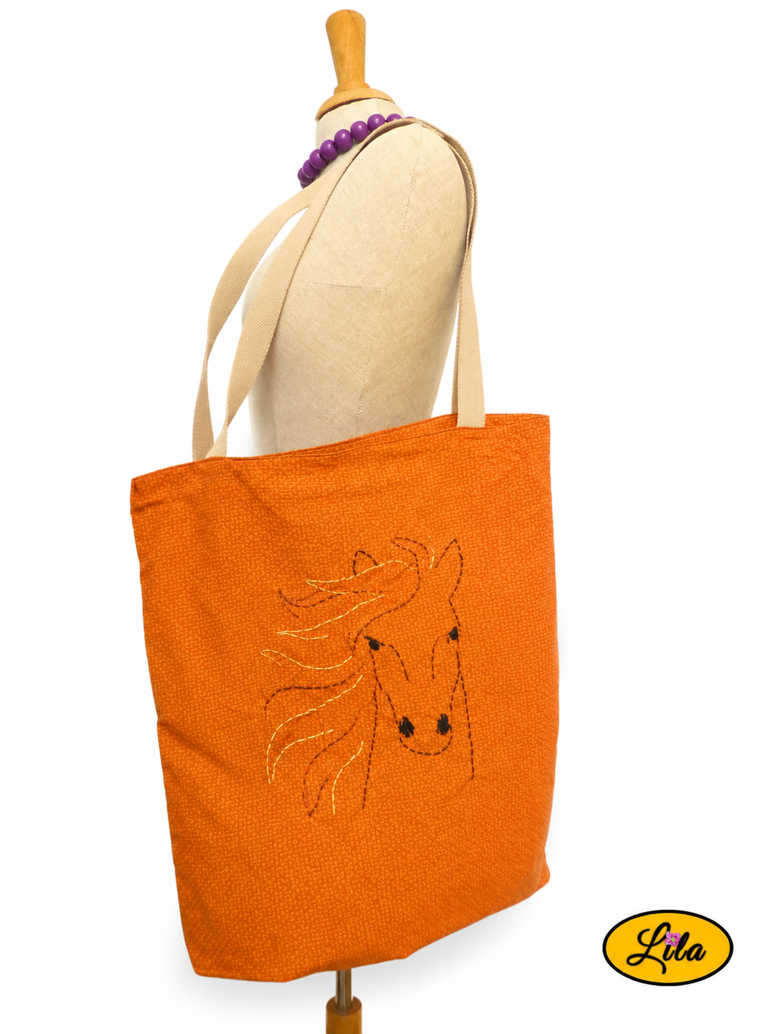 Tote bag orangé avec broderie cheval porté sur mannequin de couture sur fond blanc avec sangles couleur sable style équestre et artisanal