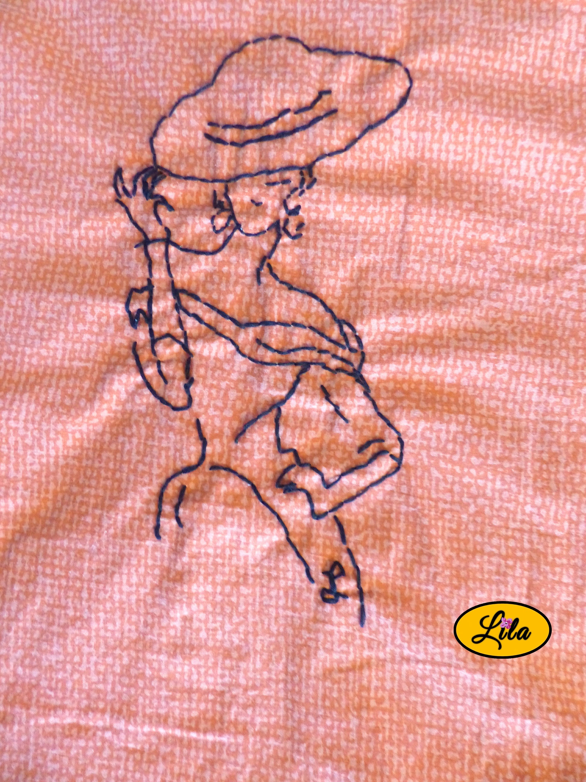 Zoom sur la broderie artisanale représentant une mannequin vintage réalisée sur un tote bag orangé mettant en valeur les détails de la broderie et les finitions faites main