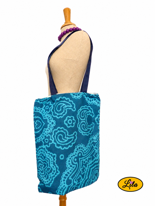 Tote bag en tissu bleu turquoise à motifs graphiques bleus porté sur mannequin de couture sur fond blanc style moderne et artisanal