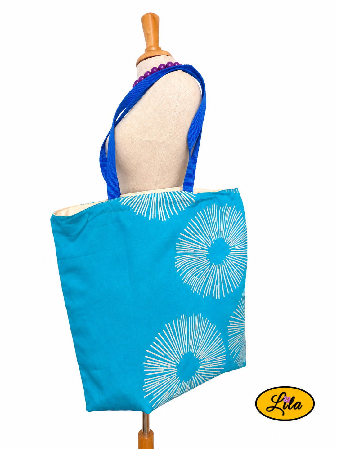 Tote bag bleu turquoise décoré de trois soleils géométriques argentés porté sur mannequin de couture sur fond blanc style contemporain et artisanal