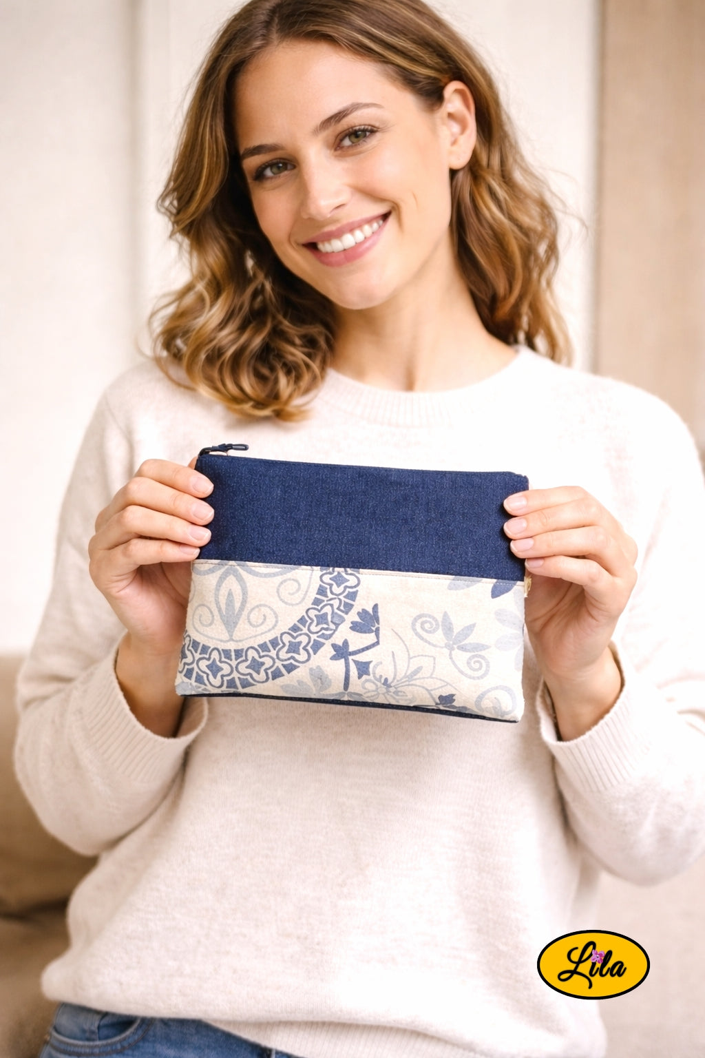 Trousse en jeans avec bande blanche à motifs bleus tenue à deux mains par une jeune fille souriante face caméra style casual et tendance