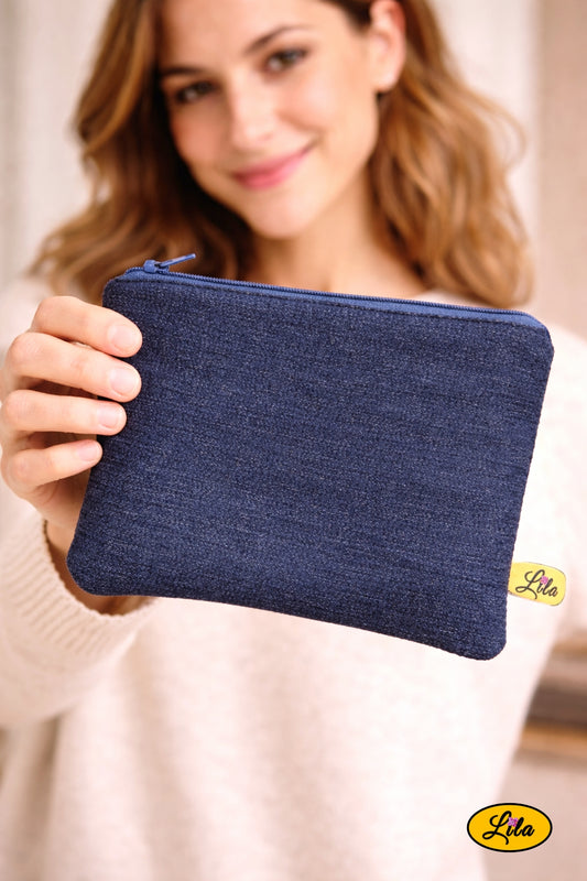 Trousse en jeans foncé tenue à une main par une jeune femme tendant la trousse en premier plan vers l’objectif style casual et moderne