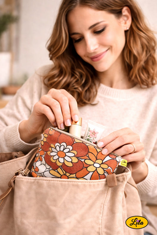 Trousse vintage orange fleurie utilisée par une jeune femme rangeant ses affaires de maquillage avec la trousse partiellement glissée dans son sac à main posé sur son bureau style bohème et féminin